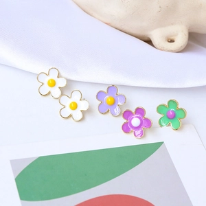 Detail von bunten Blumen-Ohrsteckern in Weiß und Lila mit Goldrand und Emaille-Finish