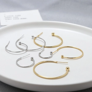 Minimalist gold and silver C-shaped hoop earrings in various sizes on a white ceramic tray