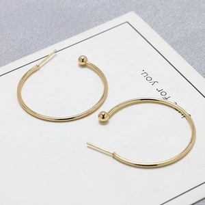 Detail of gold C-shaped hoop earrings with metal ball charm on a white display card