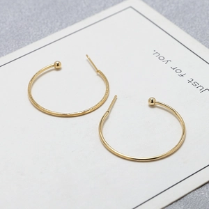Detail of gold-plated minimalist C-shaped hoop earrings with polished bead accents on white card