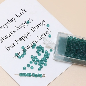 Macro shot of 3mm frosted cyan glass seed beads with clear storage box and metal pin