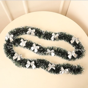 Detail of dark green Christmas tinsel garland with silver bows on a table surface