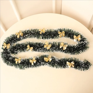 Close-up of dark green tinsel garland with snowy white edges and gold bows decor