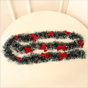Detail of dark green Christmas tinsel with white tips and red bows on a table