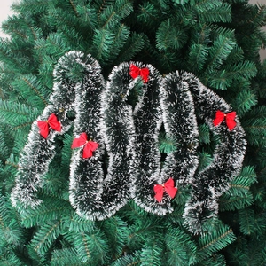 Close-up of dark green tinsel garland with snow effect tips and red satin bows decoration