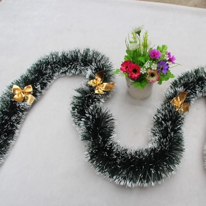Detail of dark green Christmas tinsel with white tips and shiny gold bows on plush fabric