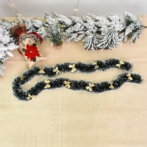 Dark green Christmas tinsel garland with white snow tips and golden bows on burlap