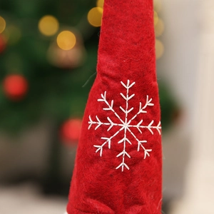 Macro shot of red felt Christmas wine cover with white embroidered snowflake detail