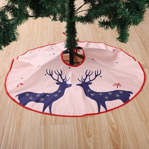 Close-up of pink Christmas tree skirt with blue reindeer pattern and red trim on wood floor