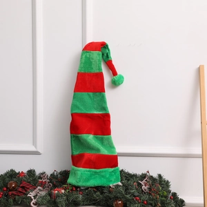 Detailed view of striped long plush Christmas elf hat with green pompom on pine branches