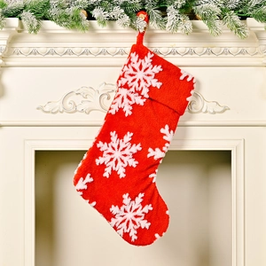 Large red plush Christmas stocking with white snowflake patterns on a fireplace