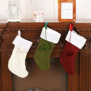 Chunky knit Christmas stockings in red, green, and white hanging on a wooden fireplace