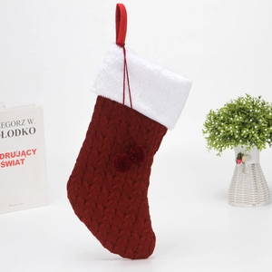 Close-up of red cable knit Christmas stocking with white plush cuff and hanging pompoms