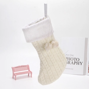 Detailed view of cream knitted Christmas stocking with white faux fur trim and soft pom-poms
