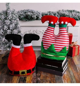 Detail view of festive Santa and elf leg hats placed by a fireplace and gift boxes
