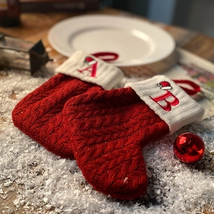 Red knit Christmas stockings with white initials A and B on a snowy wood table