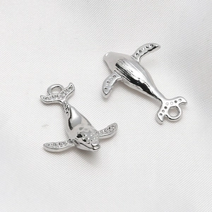Macro shot of silver whale pendants with micro-set zircons on white silk background