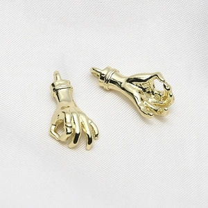 Macro shot of gold-plated OK hand gesture charms on white fabric for DIY jewelry