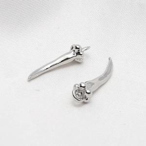 Macro shot of silver animal claw-shaped earrings on white silk fabric background