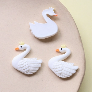 Detailed view of white swan resin charms with feather texture and golden crowns for DIY