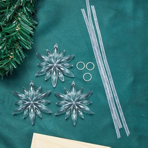 Three-piece clear acrylic snowflake ornaments set with silver ribbons on green silk background