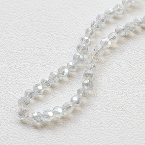 Macro shot of 4mm faceted clear crystal beads on white leather surface for DIY jewelry