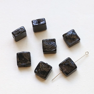 Close-up of handmade translucent black square glass beads with irregular glossy surface