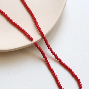 Macro shot of 3mm red faceted crystal beads on a white ceramic plate for DIY jewelry