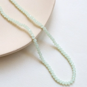 Detail of 3mm light green faceted crystal spacer beads on a cream ceramic plate