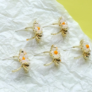 Elegantes pendientes de flores doradas con perlas blancas y centro naranja sobre papel