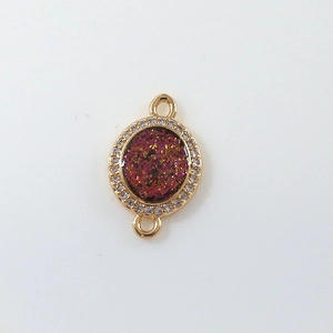 Macro detail of gold plated oval moon charm with red druzy and sparkling zircon accents