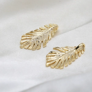 Détail de boucles d'oreilles plume dorée avec textures métalliques et tiges poussoirs