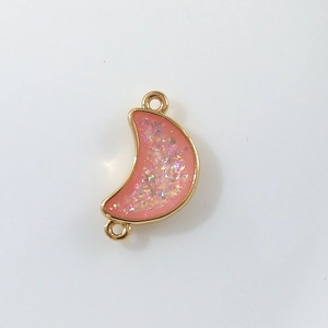 Macro shot of gold plated crescent moon pendant with pink sequins and zircon inlay