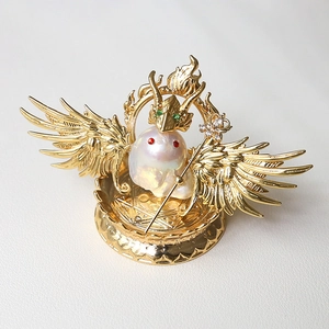 Macro detail of baroque pearl with gold wing hardware and emerald crown on leather base