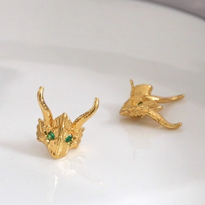 Macro detail of gold-plated dragon head earrings with green gemstone eyes and scales
