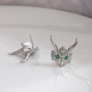 Macro detail of dragon head ear studs with green gemstone eyes and silver scales texture