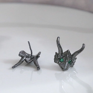 Detailed view of gunmetal dragon studs with green gemstone eyes and threaded earring backs