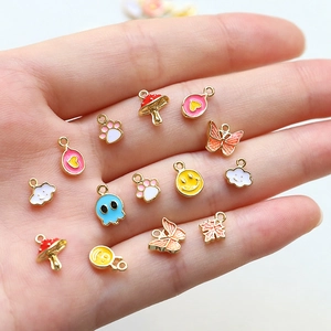 Assorted mini enamel charms including smiley faces and butterflies held in palm for scale