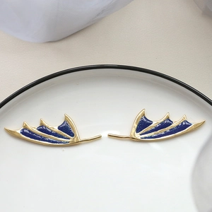 Detail of gold-plated wing earrings with dark blue enamel and glitter on white ceramic