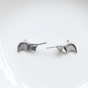 Detailed close-up of gothic silver bat wing stud earrings on a white porcelain edge
