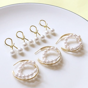 Boucles d'oreilles nœuds perles blanches et créoles dorées dans un plateau blanc