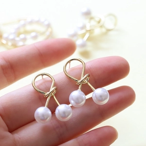 Vue macro de boucles d'oreilles nœuds en argent S925 avec perles blanches sur main