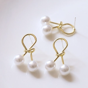 Gros plan de boucles d'oreilles nœud en or poli avec perles blanches et clous en argent S925