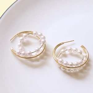 Détail macro de boucles d'oreilles nœud doré avec perles blanches et tige en argent 925