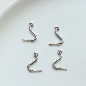 Macro shot of 4-piece silver devil tail jewelry charms with polished S-curve on white ceramic