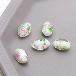 Close-up of handmade oval glass beads with pink rose pattern and gold foil accents