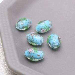 Macro view of oval glass beads with gold foil and hand-painted floral motifs for DIY jewelry
