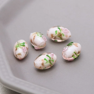 Detail of five handmade white glass oval beads with pink rose flowers and gold foil