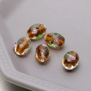 Macro shot of 5 handmade oval amber glass beads with floral gold foil patterns for DIY jewelry