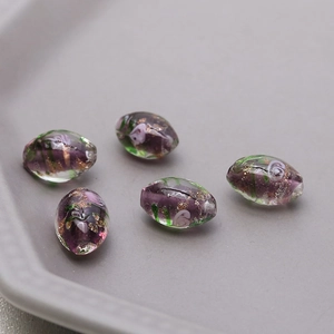 Macro shot of oval glass beads with purple core, green ribbons and gold foil details